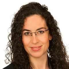 A woman with curly hair and glasses posing for a photo.