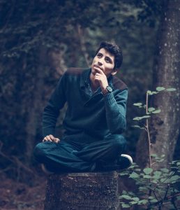 A man sitting on a stump in the woods.